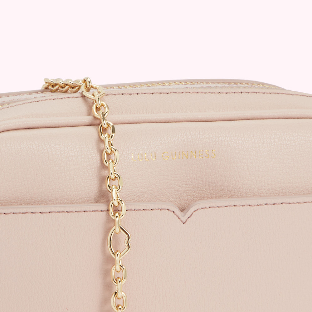 Close-up of a pale pink Lulu Guinness crossbody bag with a gold chain strap.