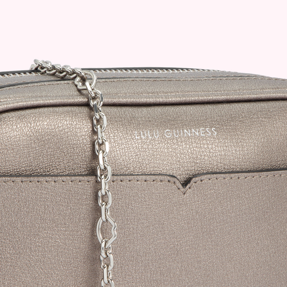 Close-up of a silver Lulu Guinness crossbody bag with a chain strap.
