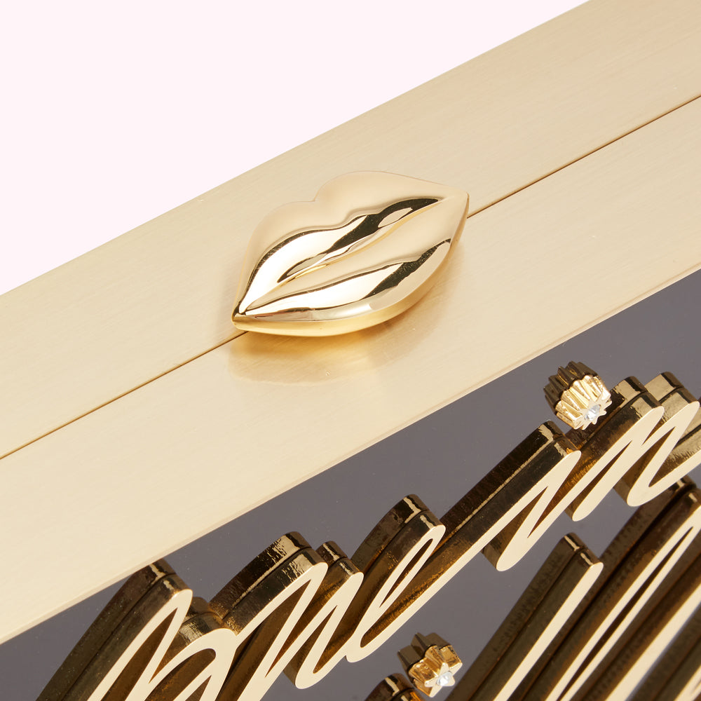 Close-up of a gold clutch with a gold lip-shaped clasp and the word "love" engraved on a dark background.
