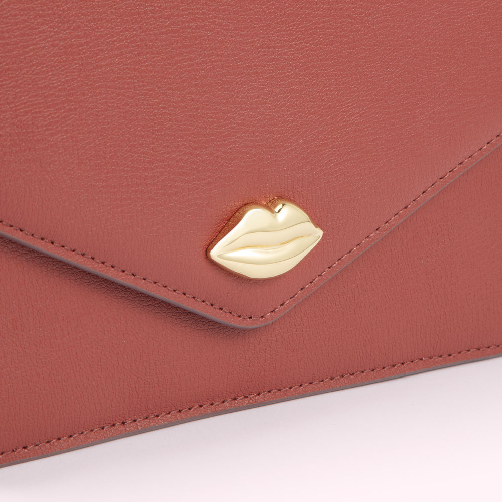 Close-up of a dusty rose leather envelope-style bag with a gold lip detail.
