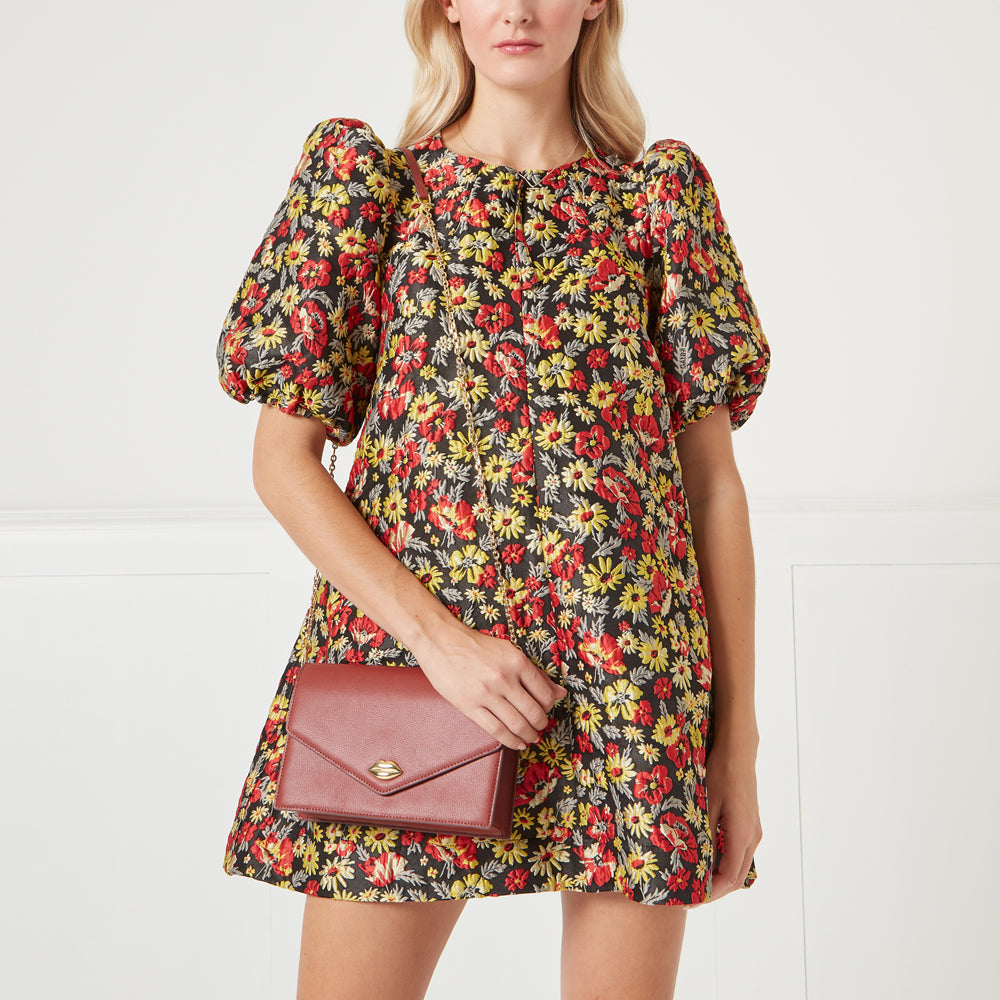 Woman in floral dress holding a burgundy crossbody bag.