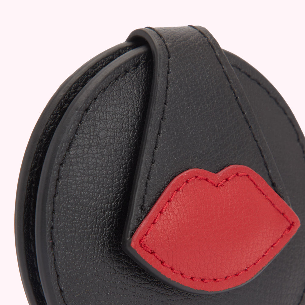 Close-up of a black leather compact mirror with a red leather lip detail.
