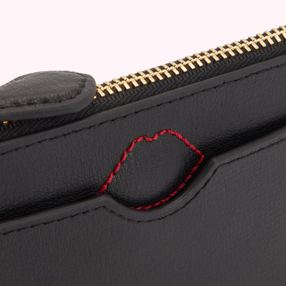 Close-up of a black leather wallet with a red stitched lip detail and gold zipper.
