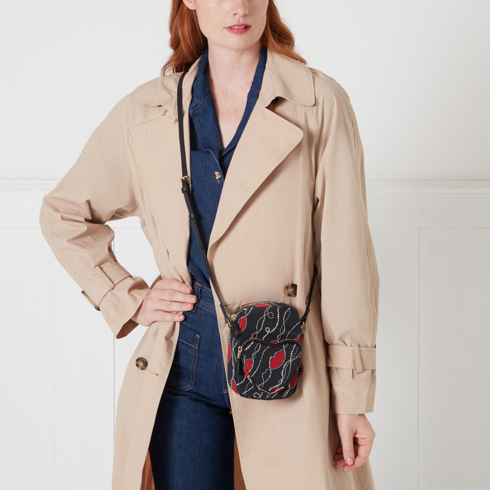 Woman in beige trench coat wearing a small black crossbody bag with a red and gold lip print.

