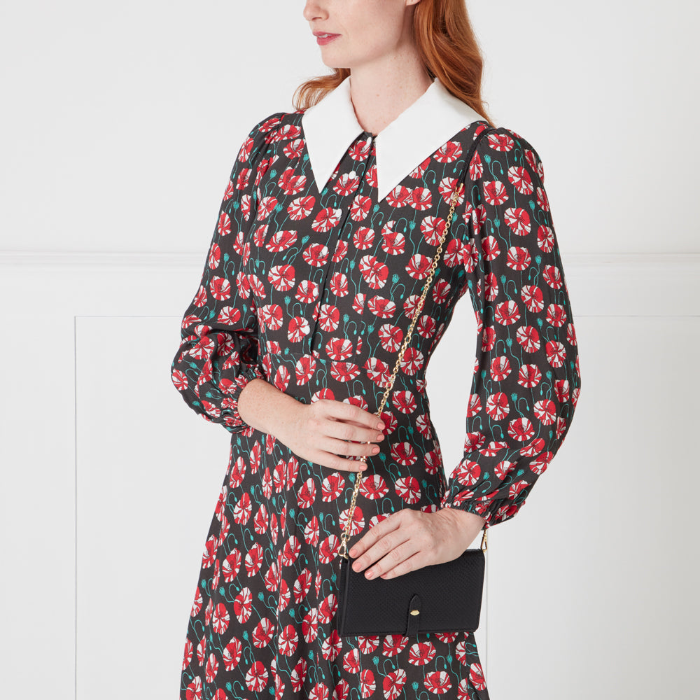 A woman in a poppy-print dress holds a black chain-strap wallet.
