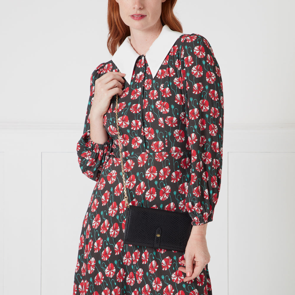 Woman in a red and black floral dress holding a black chain purse.
