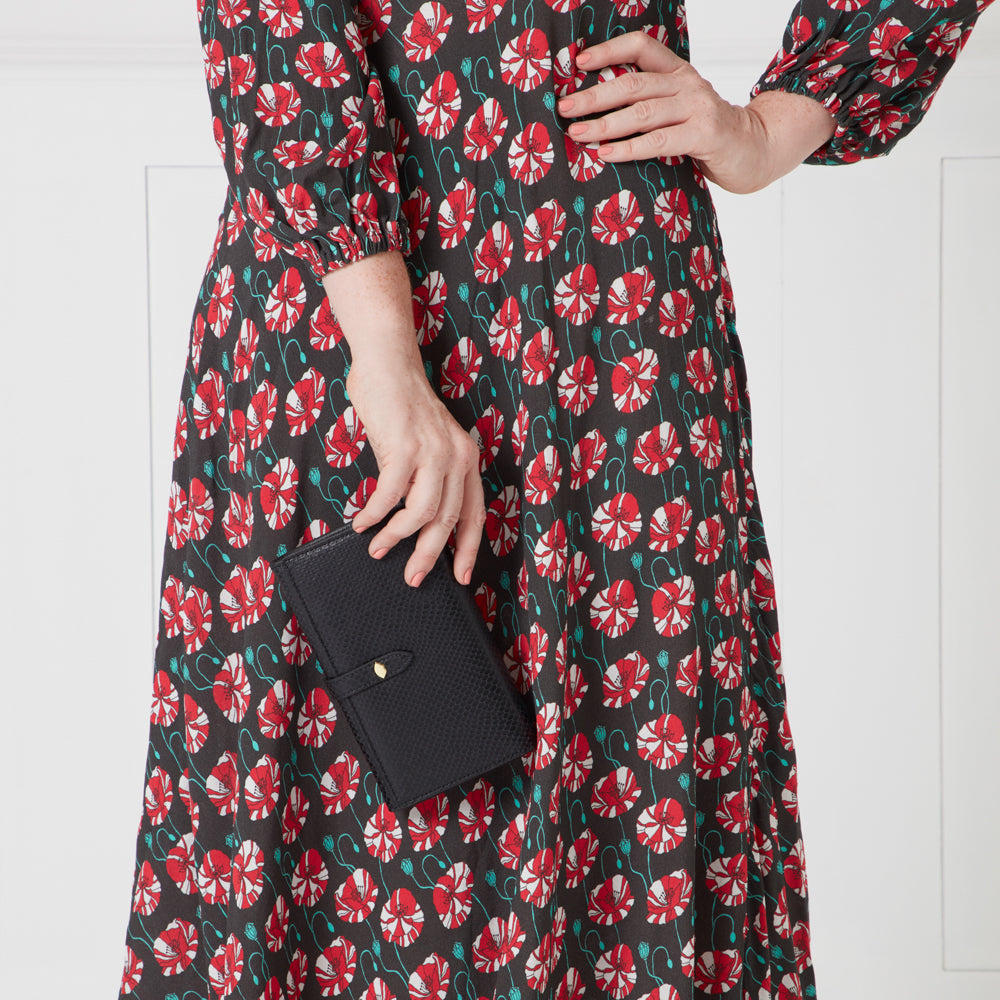 Woman in a dark floral dress holding a black leather wallet.
