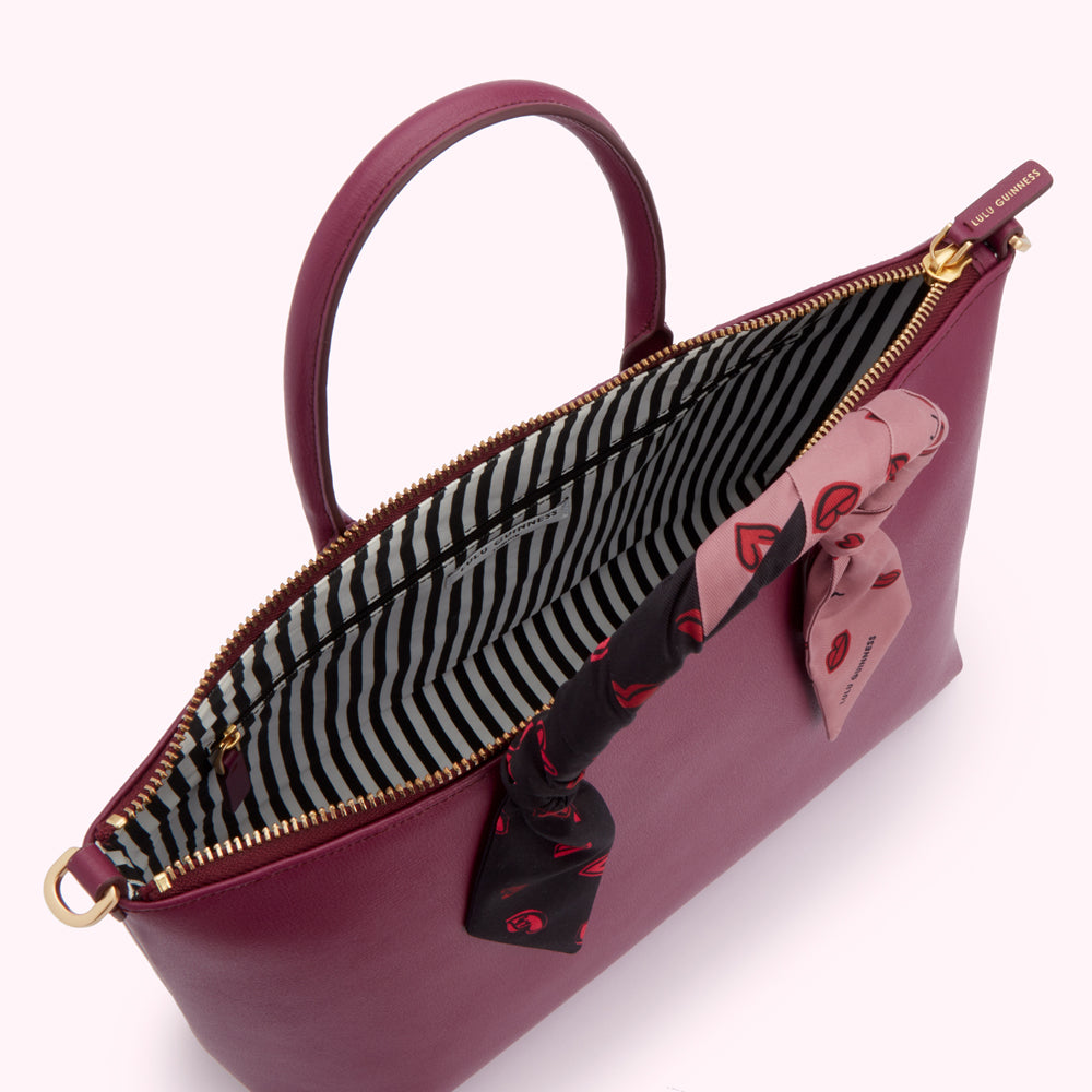 Overhead view of a burgundy Lulu Guinness satchel with a black and pink heart print scarf inside.
