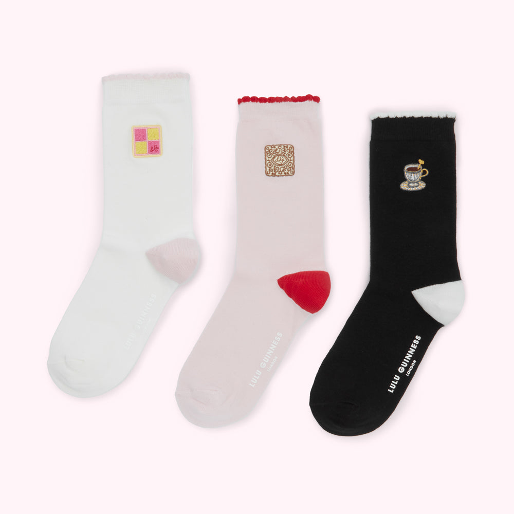 Three pairs of Lulu Guinness socks with embroidered images of a pink and yellow biscuit, a brown biscuit, and a cup and saucer.
