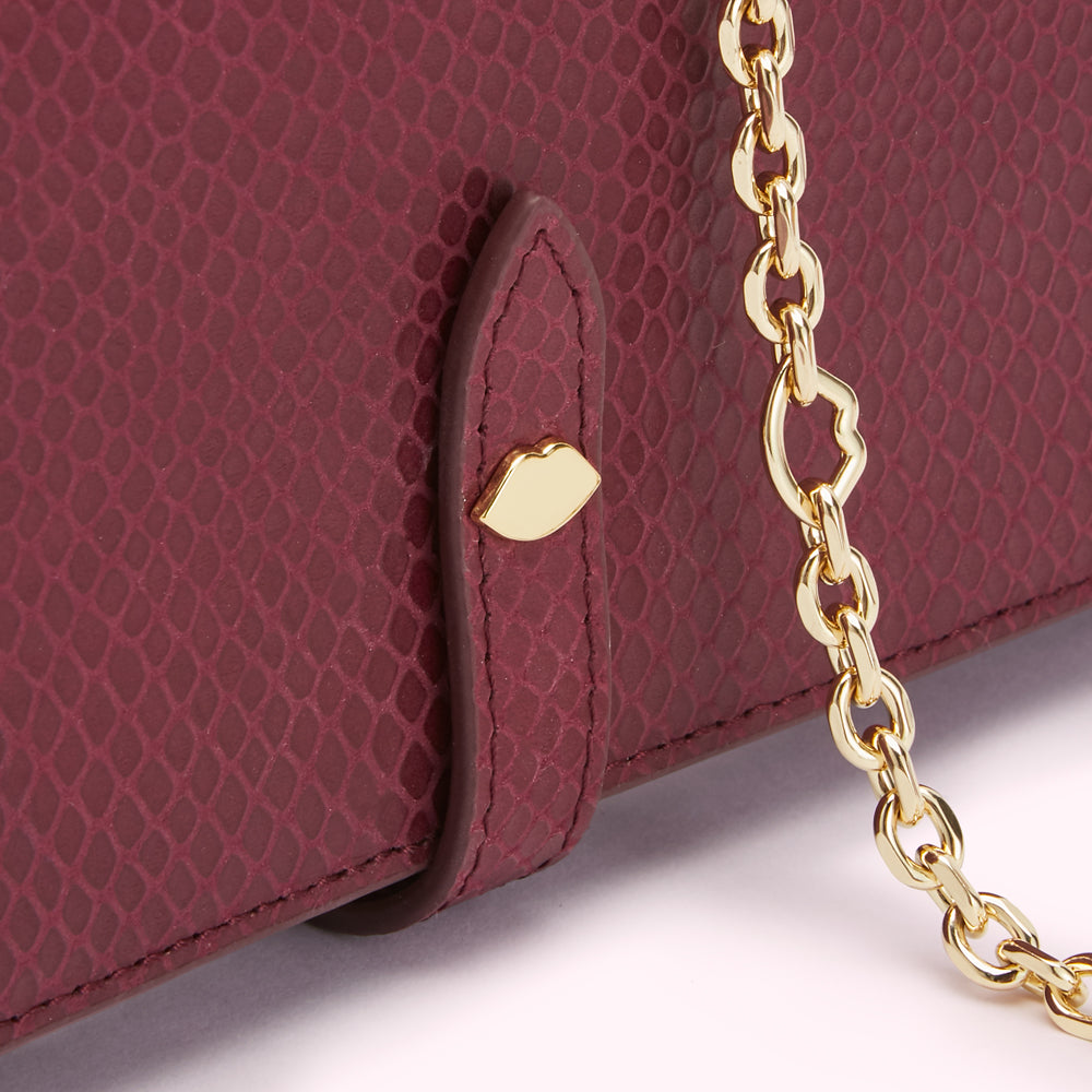 Close-up of a burgundy snakeskin-textured wallet with a gold chain and lip-shaped clasp.