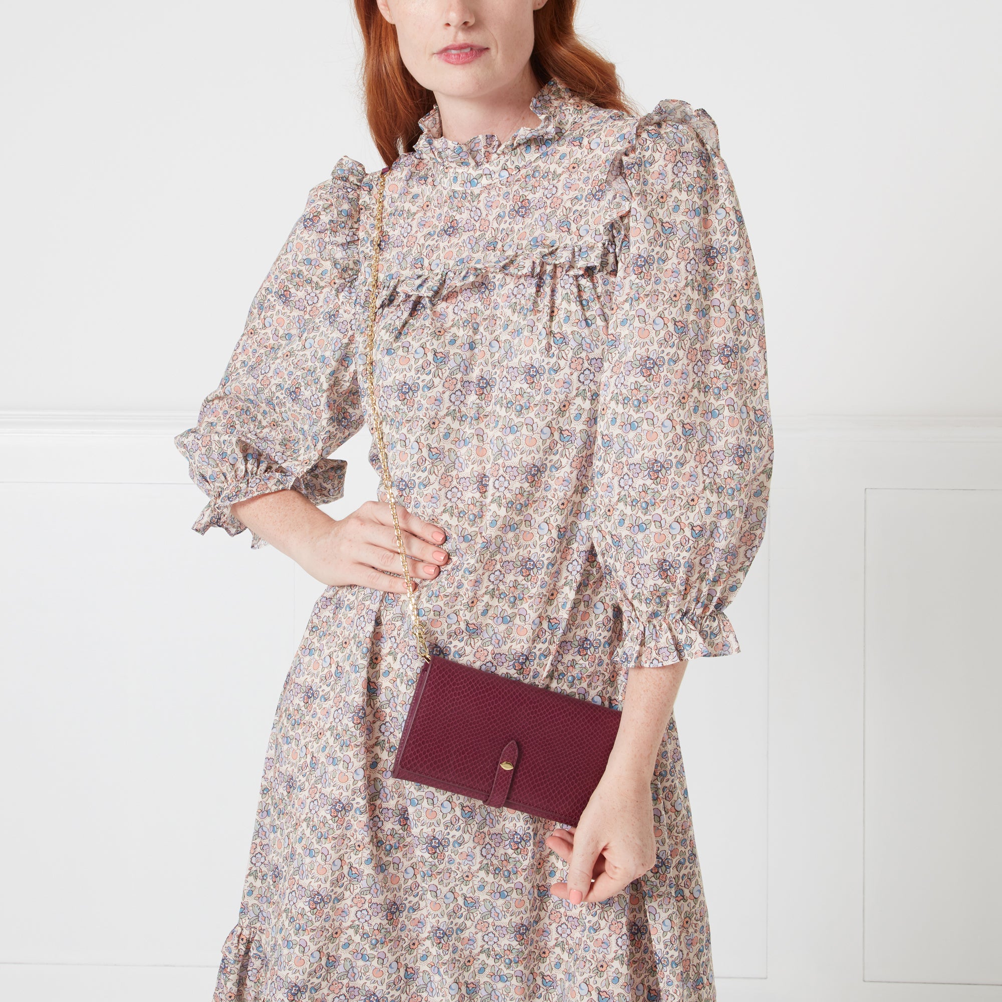 A woman in a floral dress holds a burgundy chain wallet.

