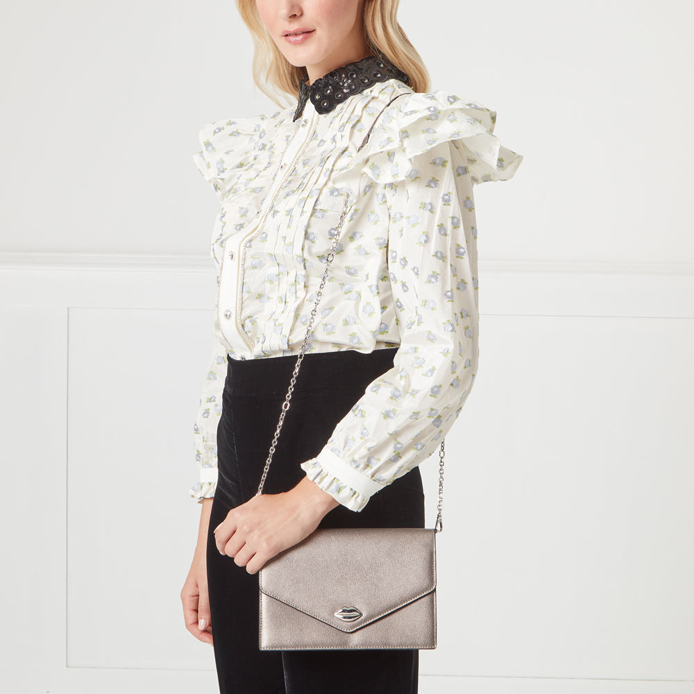 Woman wearing a white floral blouse and black pants holding a silver crossbody bag.
