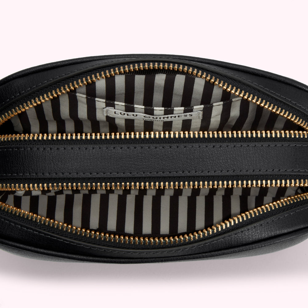 Overhead close-up of the inside of a black Lulu Guinness crossbody bag with gold zippers and a black and white striped lining.
