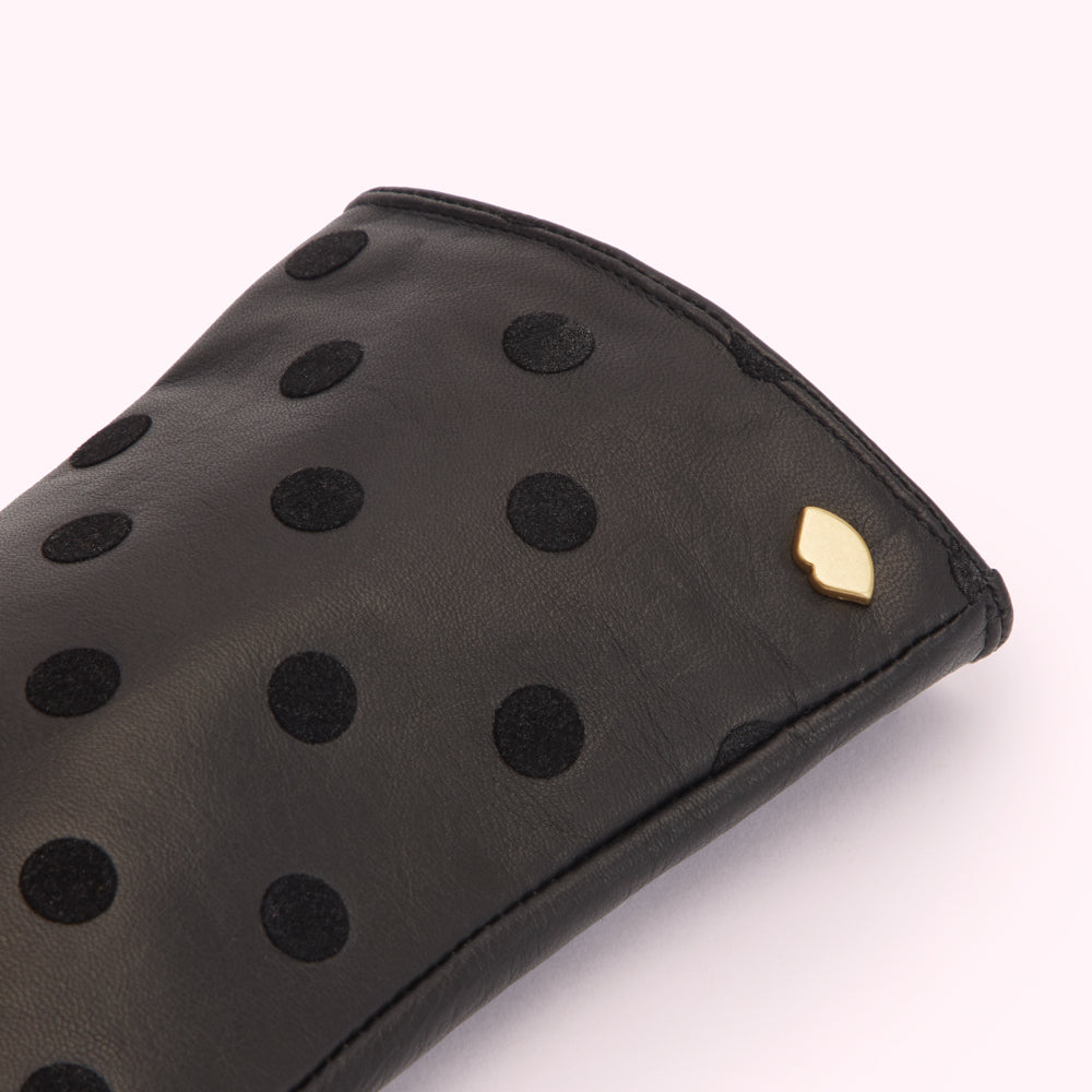 Close-up of a black leather glove with black polka dots and a small gold logo.
