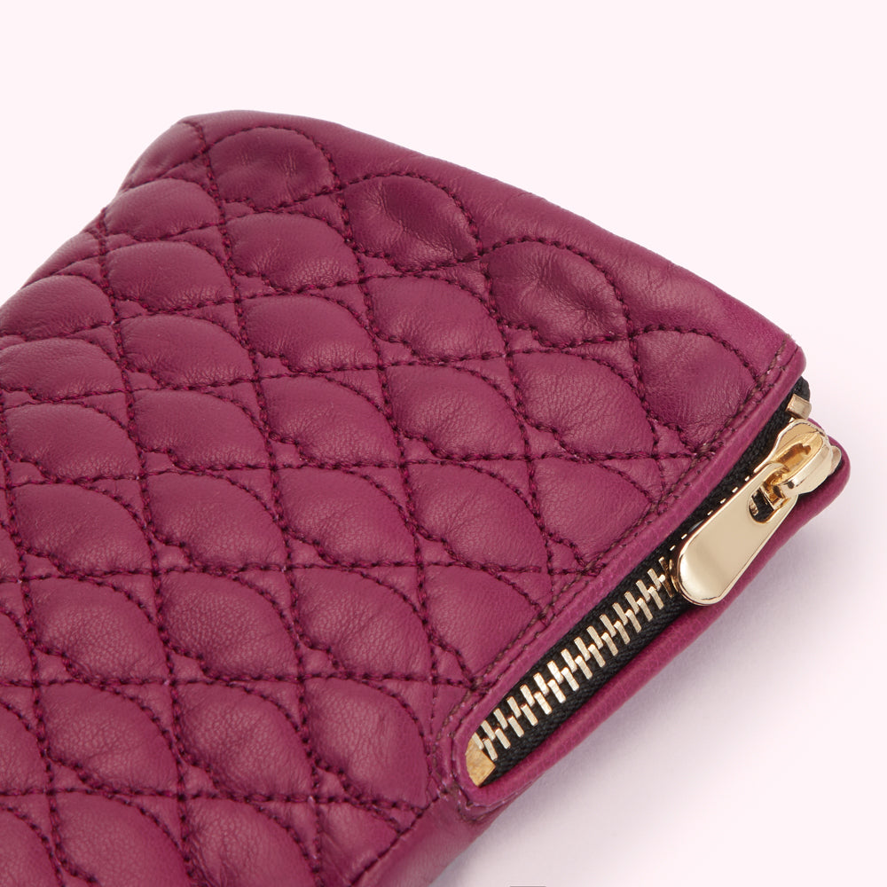 Close-up of a quilted burgundy leather clutch with a gold zipper.
