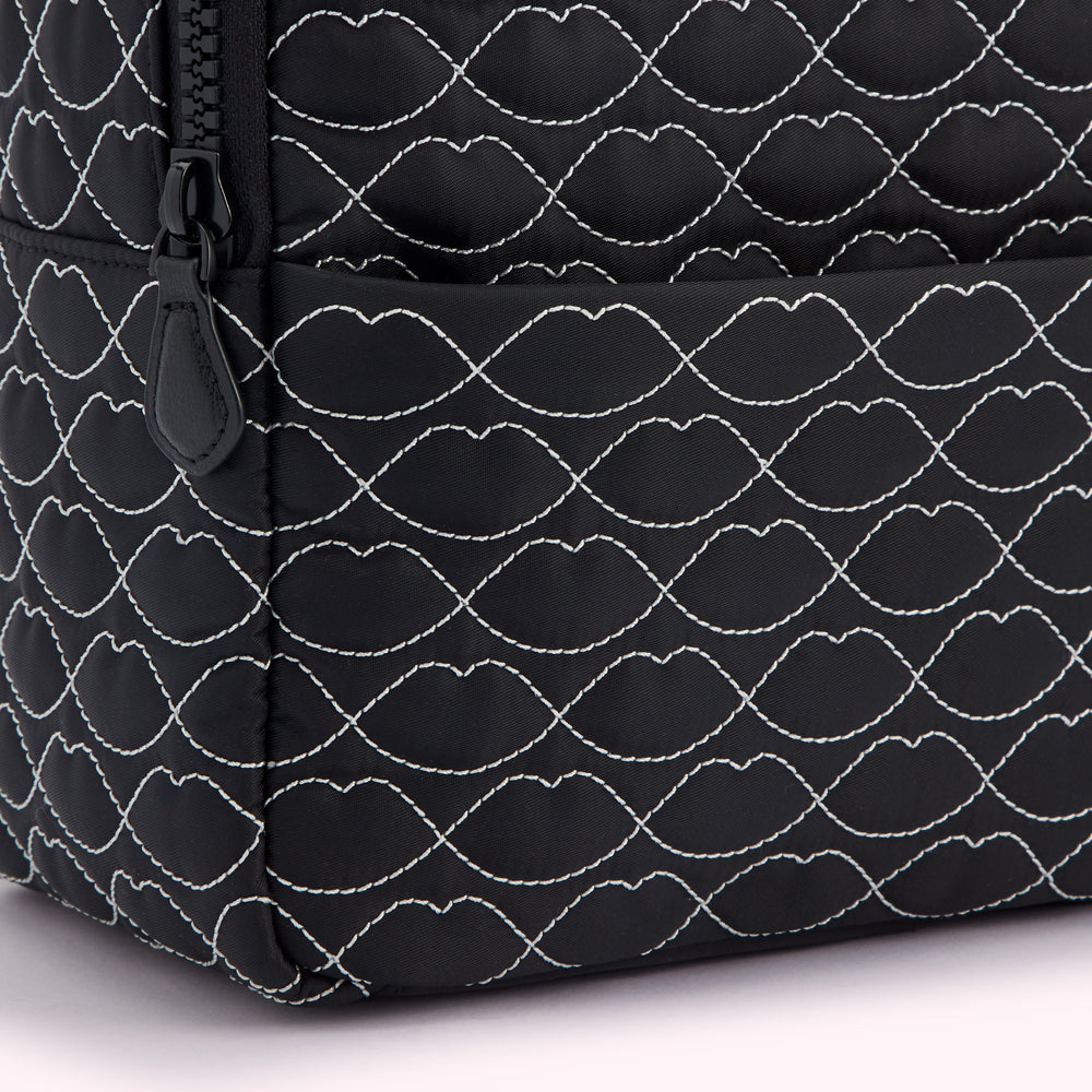 Close-up of a black quilted backpack with a lip-shaped pattern.
