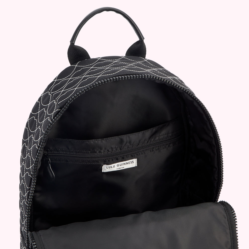 Open black Lulu Guinness quilted backpack with white stitching, showing the interior lining and a label.
