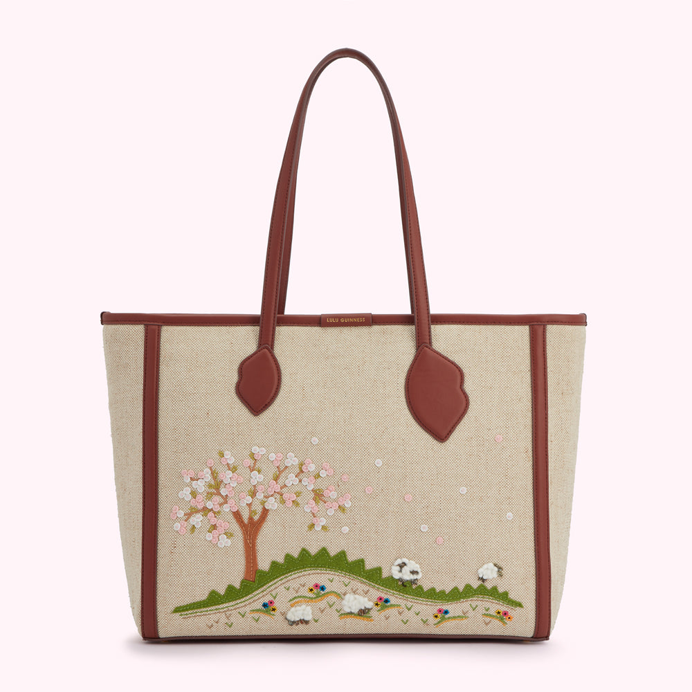 Beige tote bag with brown leather trim and embroidered cherry blossom tree and sheep scene.