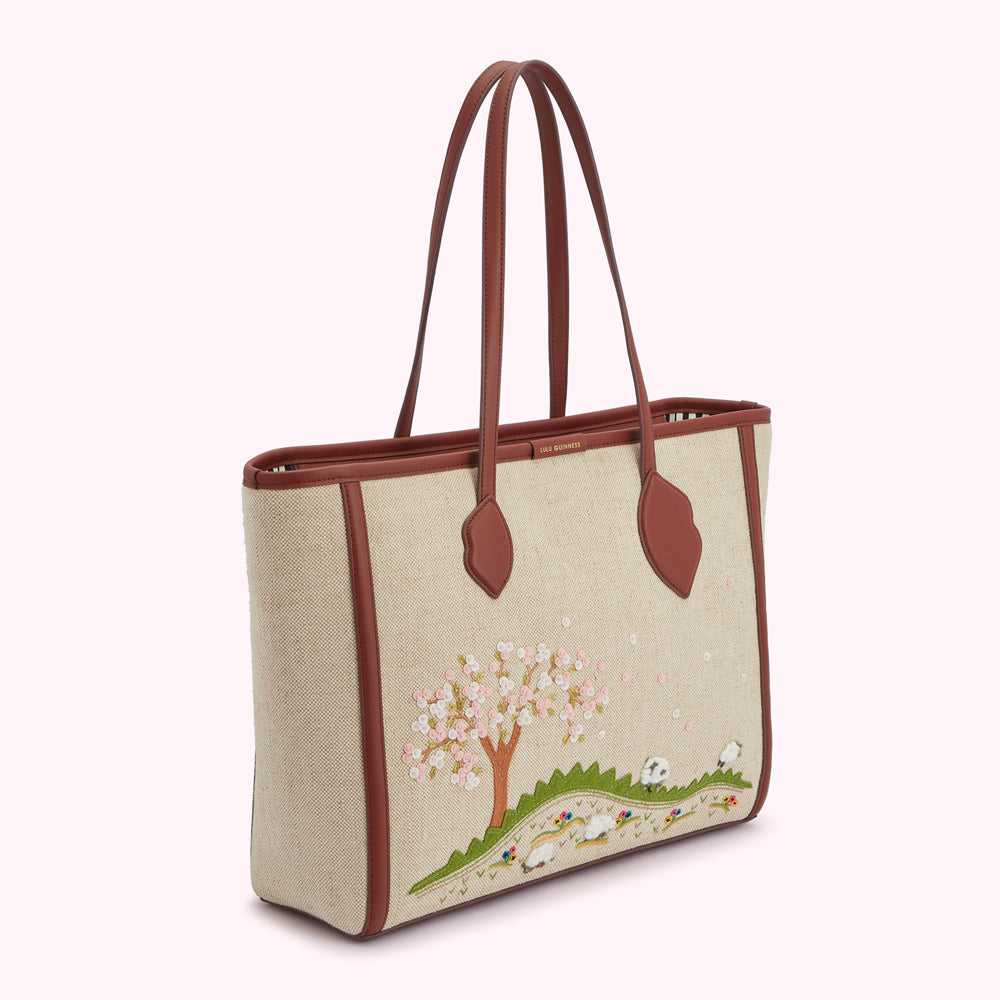 Beige tote bag with brown leather trim and embroidered cherry blossom tree and sheep design.