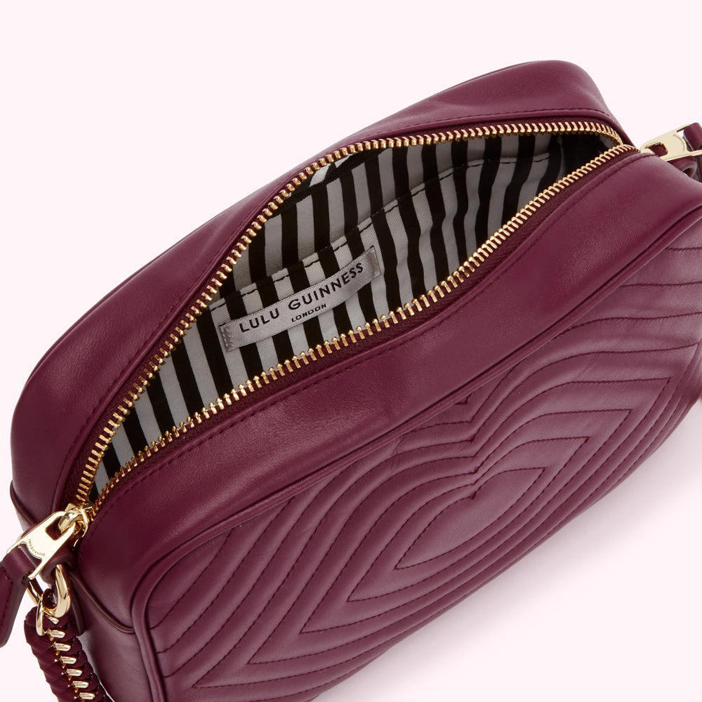 Burgundy quilted Lulu Guinness crossbody bag with gold zipper and braided strap, open to reveal a black and white striped interior.