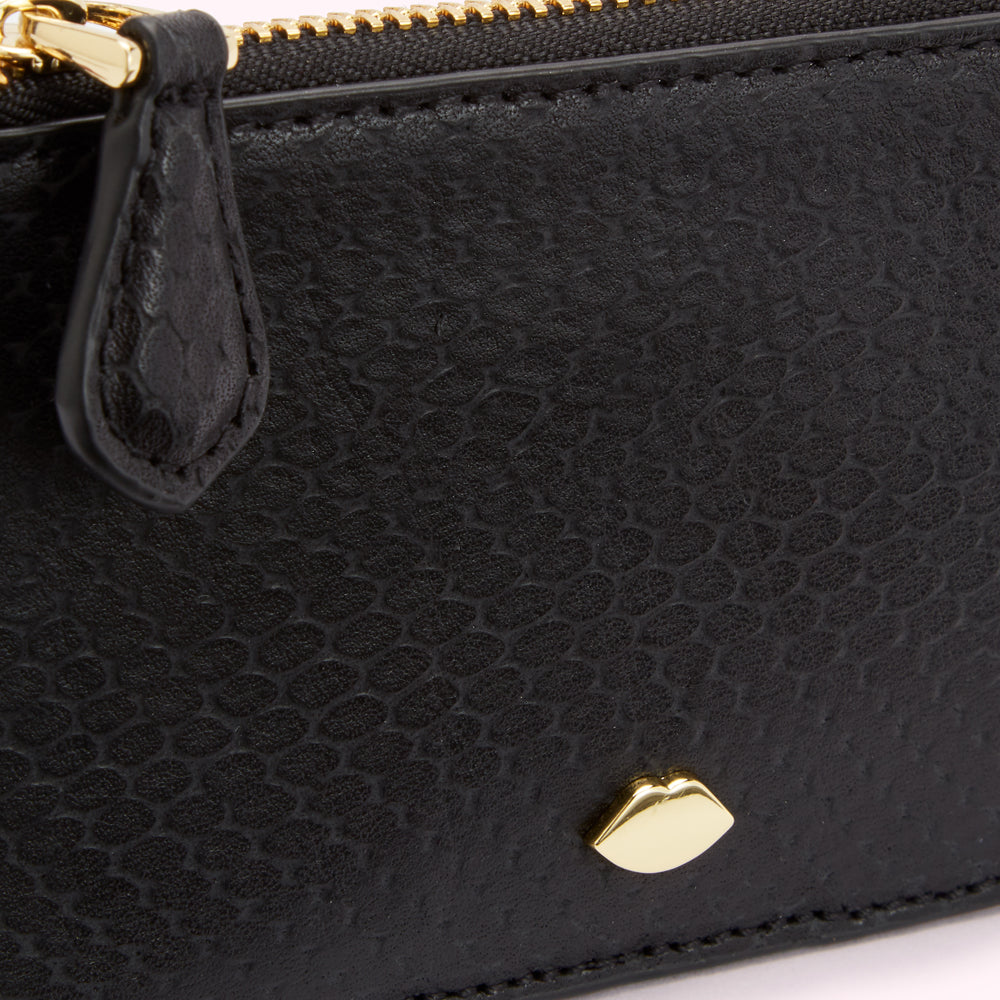 Close-up of a black leather zip-around wallet with a gold lip-shaped logo.
