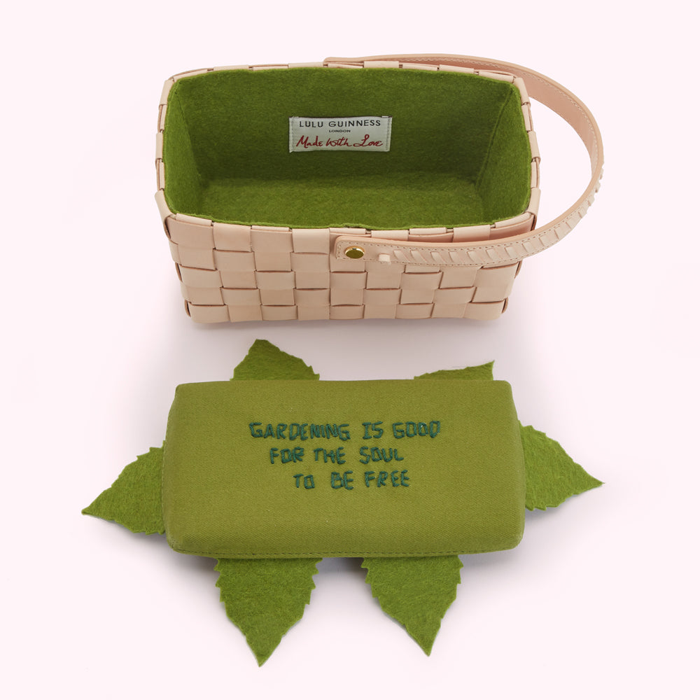 A pale pink woven basket with a green felt lining, which features a label reading "Lulu Guinness London, Made with Love", is shown alongside a green felt insert with the words "Gardening is good for the soul to be free" embroidered on it and decorated with green felt leaves.