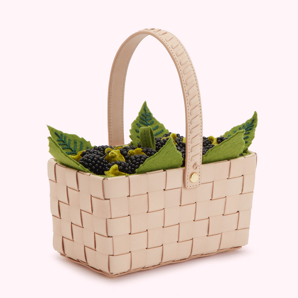 Beige leather woven basket filled with felt blackberries and green leaves.