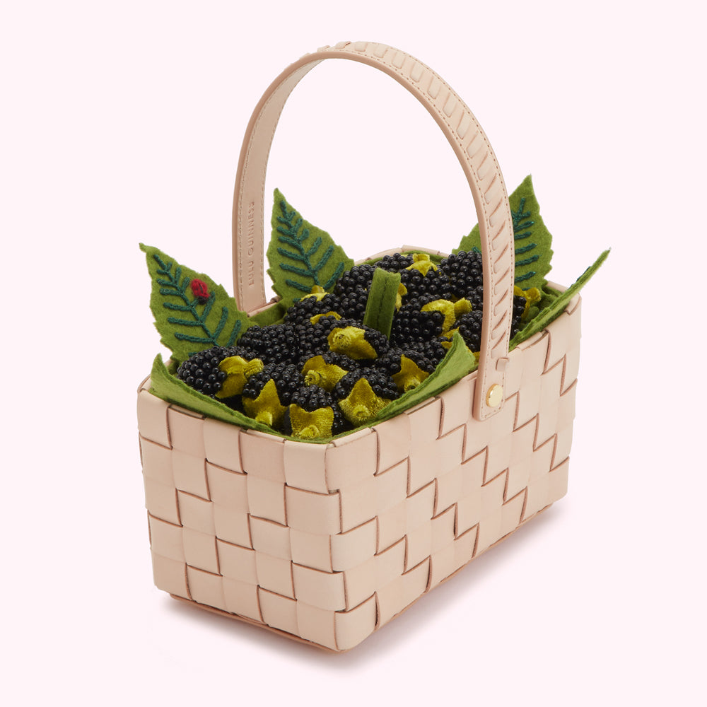A beige woven leather basket filled with black and green felt blackberries and green felt leaves; a small ladybug is embroidered on one leaf.