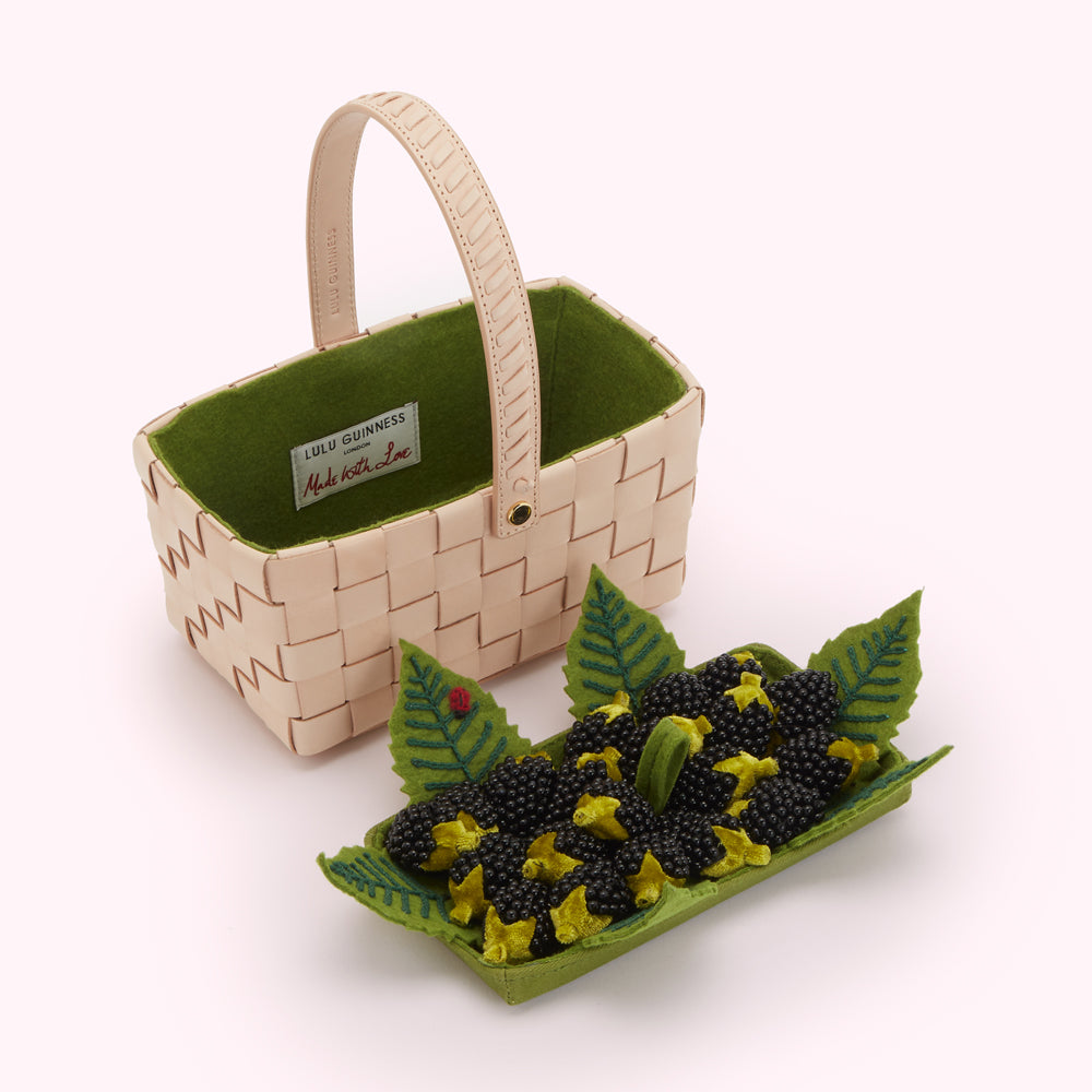 A pale pink woven leather basket with a green felt lining containing a tray of felt blackberries.