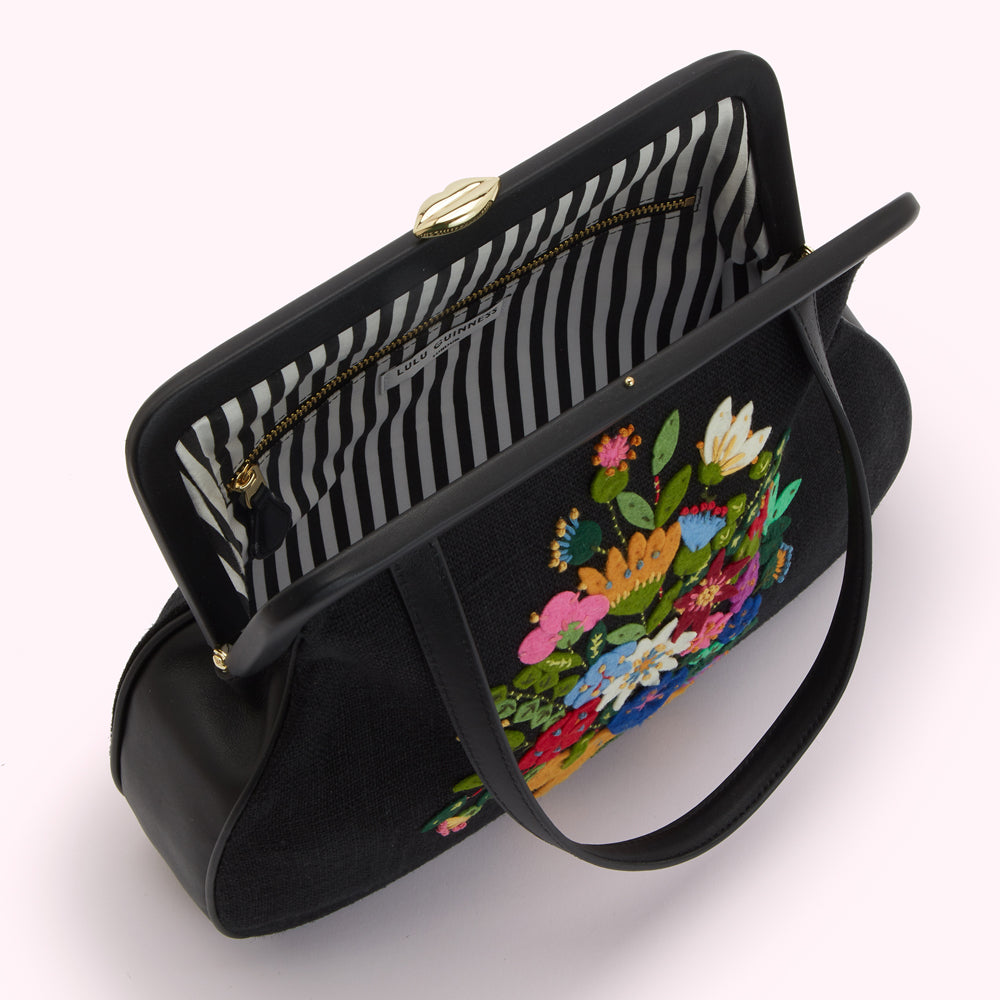 Overhead view of a black Lulu Guinness handbag with a colourful embroidered floral bouquet and a black and white striped interior.