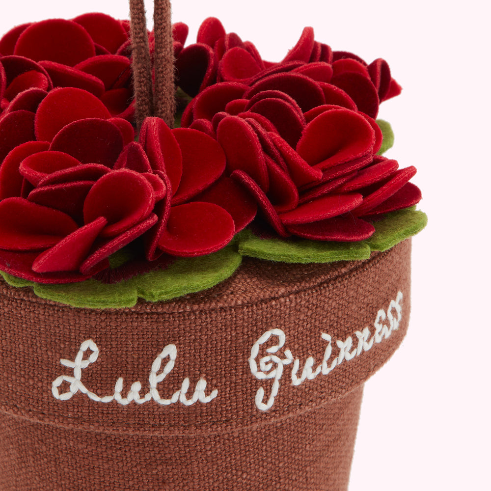 Close-up of a small brown fabric pot with embroidered text "Lulu Guinness" and a felt flower arrangement in dark red.
