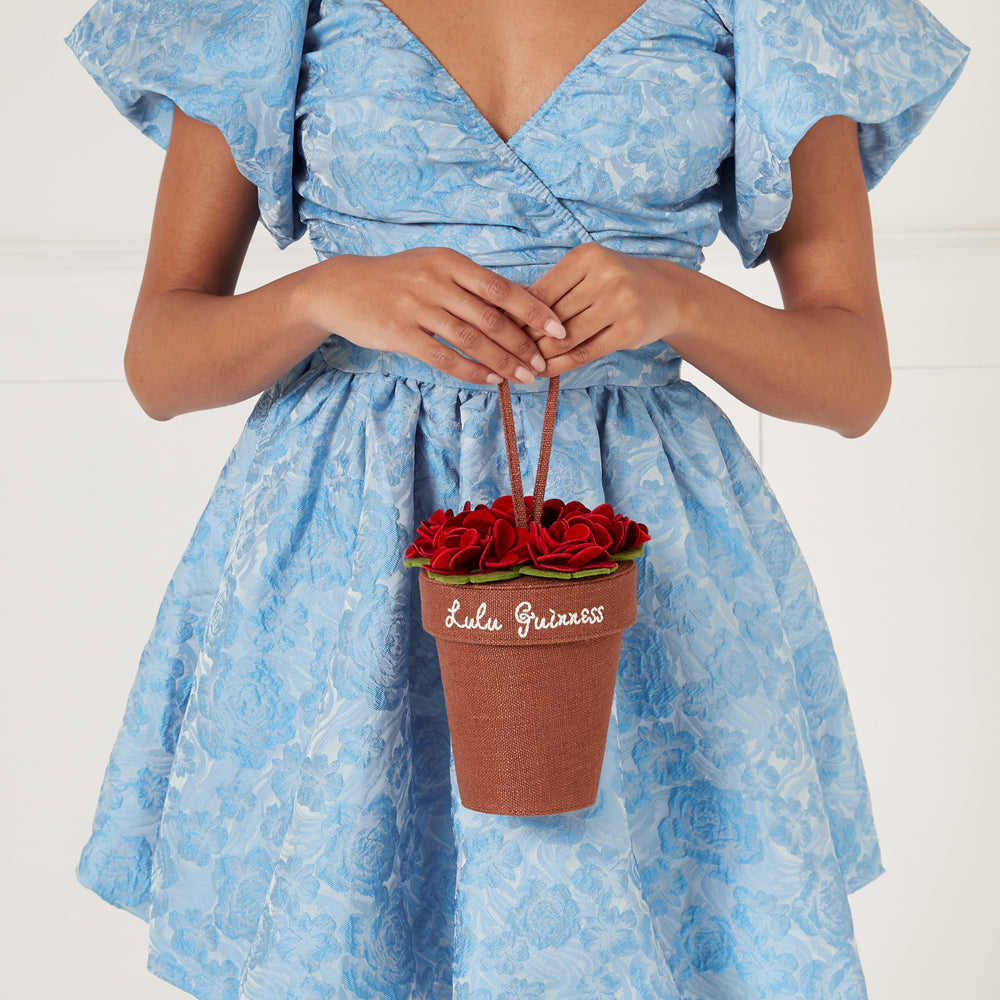 Woman in a light blue dress holding a brown Lulu Guinness flowerpot bag.