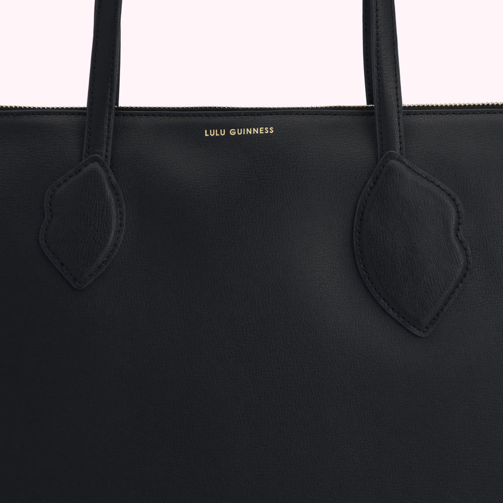 Close-up of a black Lulu Guinness tote bag's top section, showing the brand logo and textured leather.
