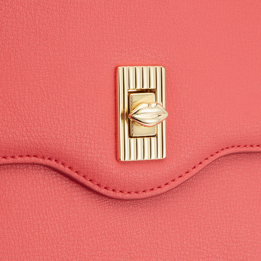 Close-up of a coral-coloured handbag's clasp, featuring a gold lip-shaped detail.
