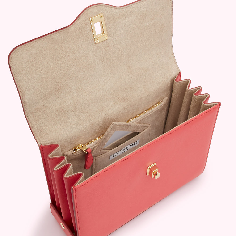 Open coral Lulu Guinness handbag showing beige interior with multiple compartments and gold hardware.