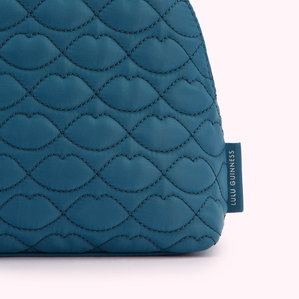 Close-up of a teal quilted Lulu Guinness makeup bag with a lip print pattern.
