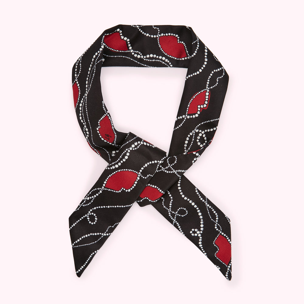 Black silk scarf with red hearts and white pearl detailing, tied in a knot.
