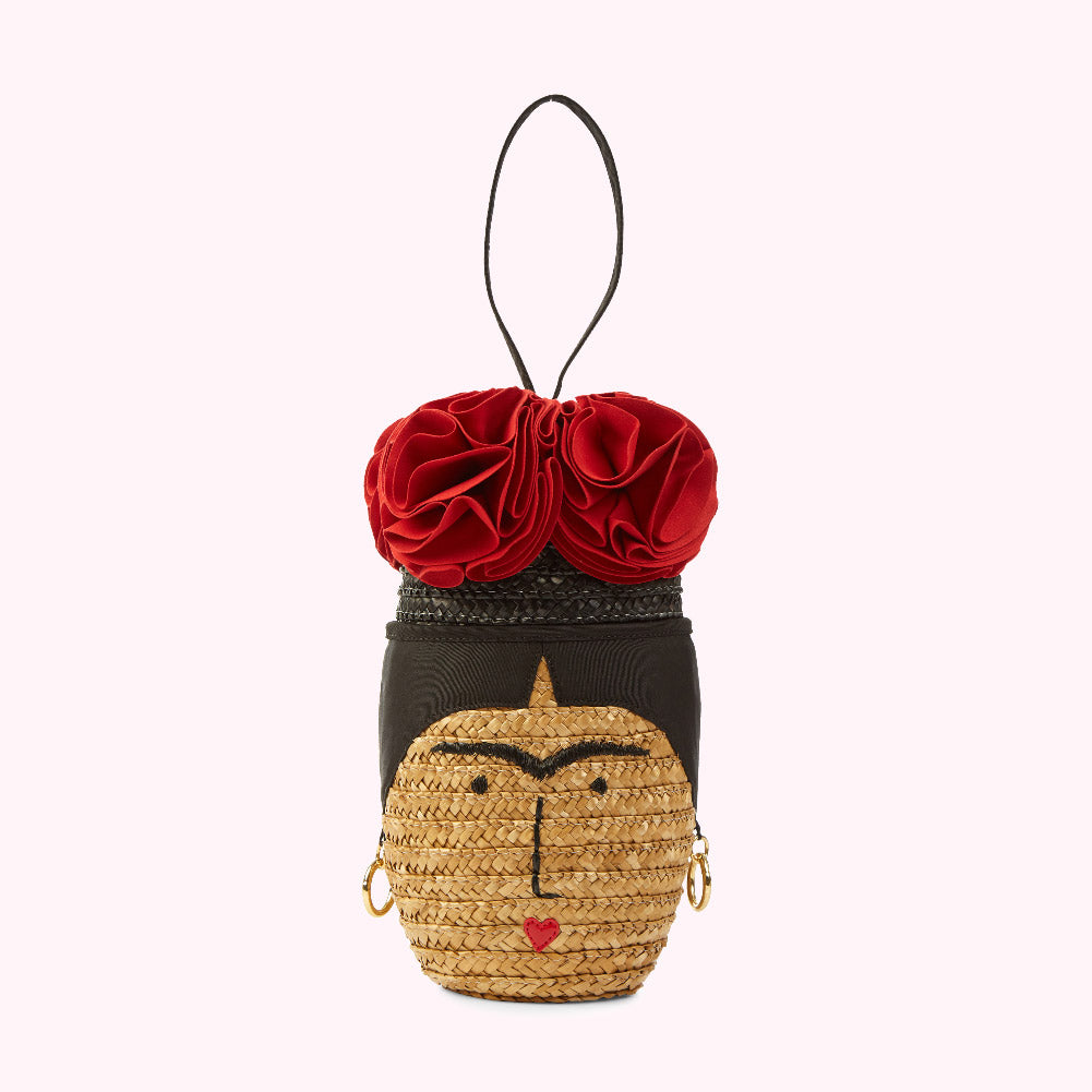 Straw bag shaped like Frida Kahlo's face, with red flowers on top and a small red heart on her chin. The background is white.
