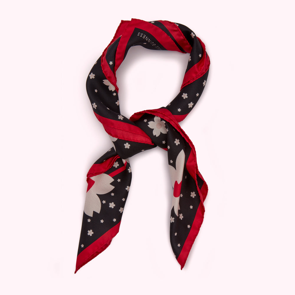 Black silk scarf with a red border and a pattern of light grey flowers.