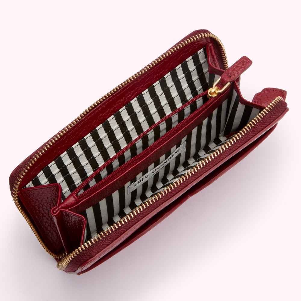 Open red leather Lulu Guinness zip-around wallet with black and white striped interior.
