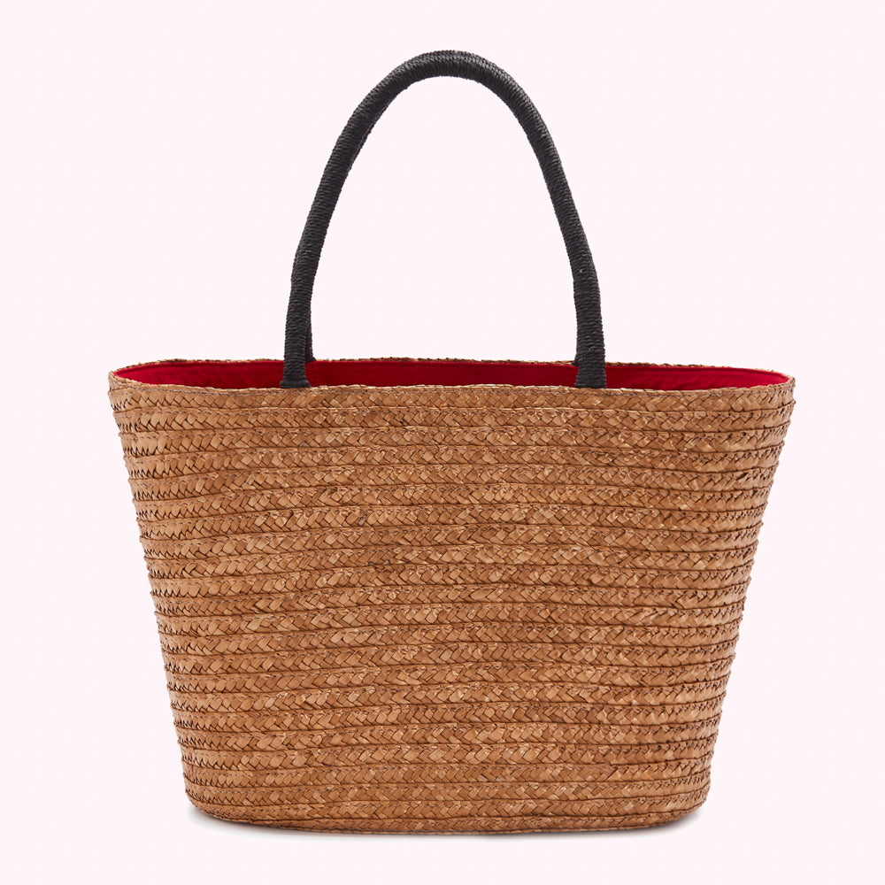 A light brown woven straw tote bag with black handles and a red interior lining, shown against a white background.
