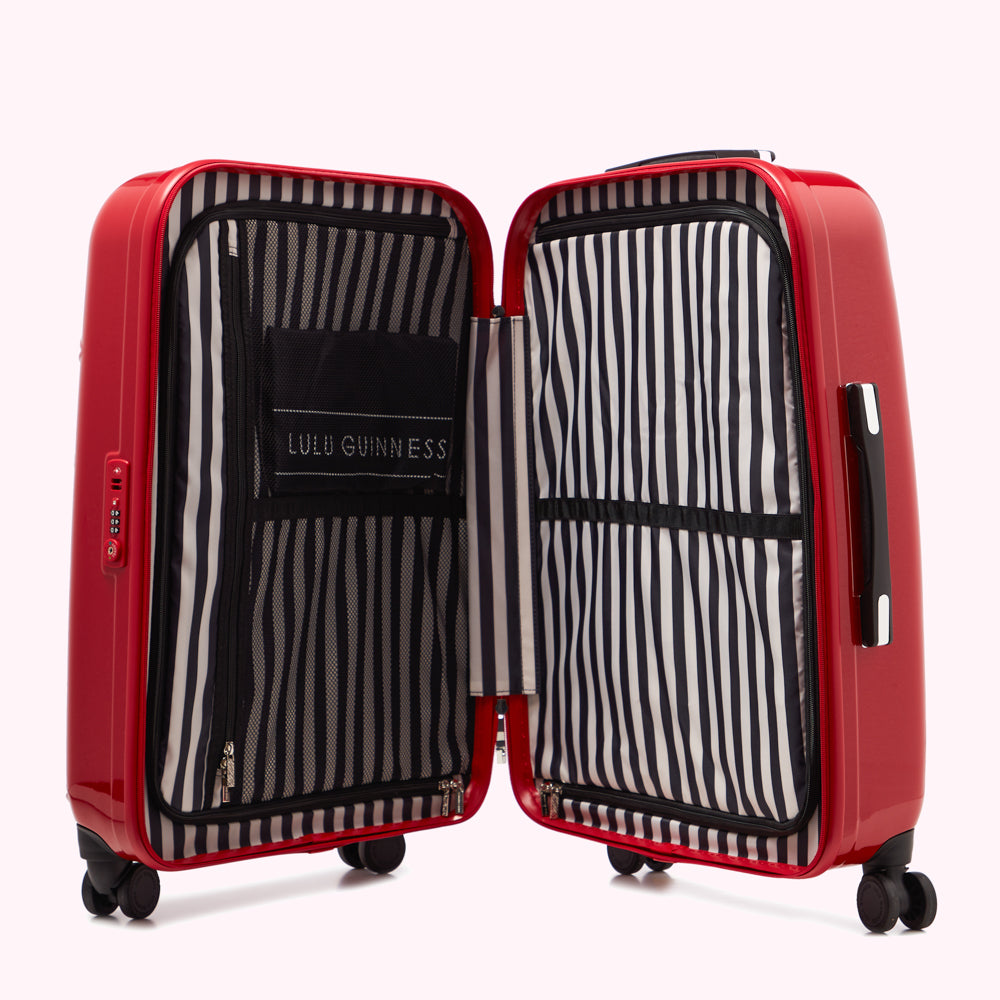 Open red Lulu Guinness suitcase with black and white striped interior lining against a white background.