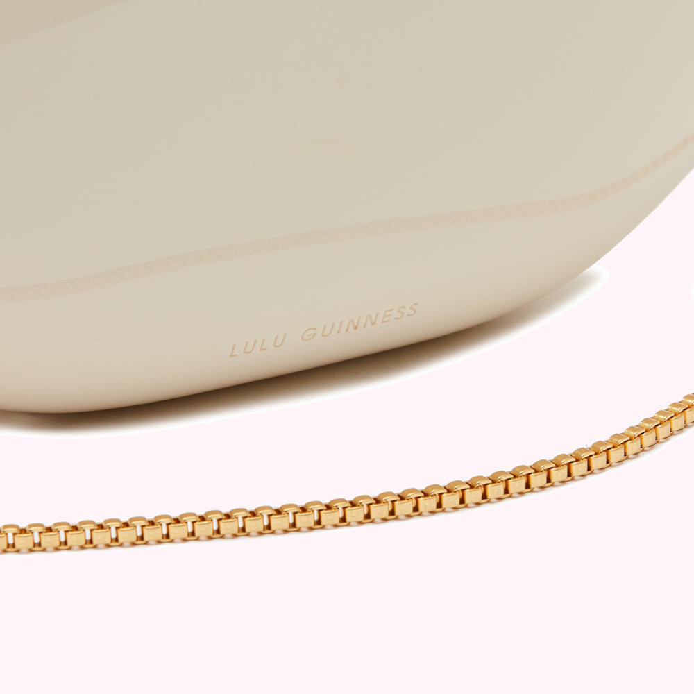 Close-up of a cream-colored Lulu Guinness bag with a gold chain strap.
