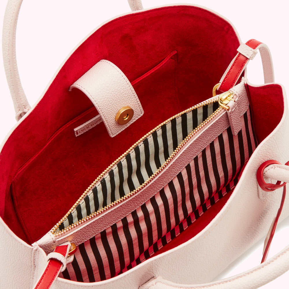 Inside of a blush pink leather handbag with a red interior and black and pink striped zippered pocket.
