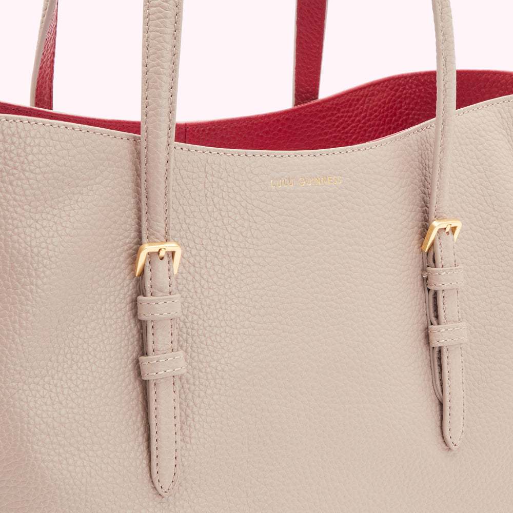 Close-up of a beige Lulu Guinness tote bag with red interior and gold buckles.
