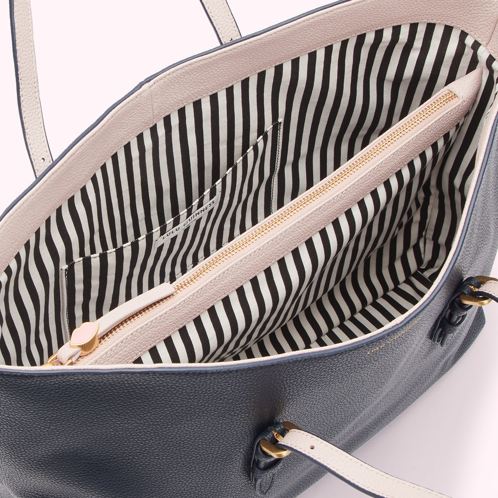 Interior of a navy blue Lulu Guinness tote bag with a blush pink zipper and black and white striped lining.