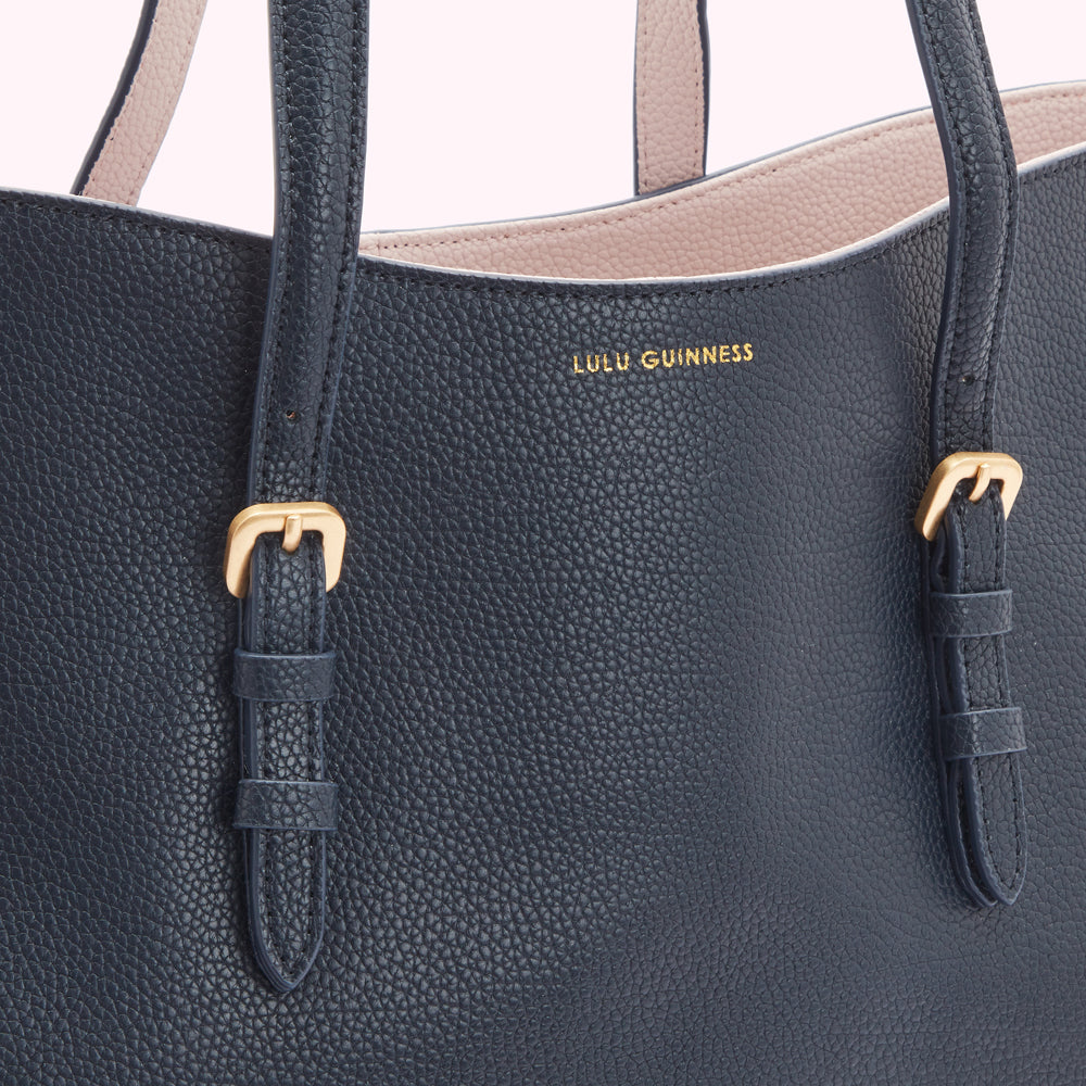 Close-up of a navy blue Lulu Guinness tote bag with pale pink interior and gold buckles.
