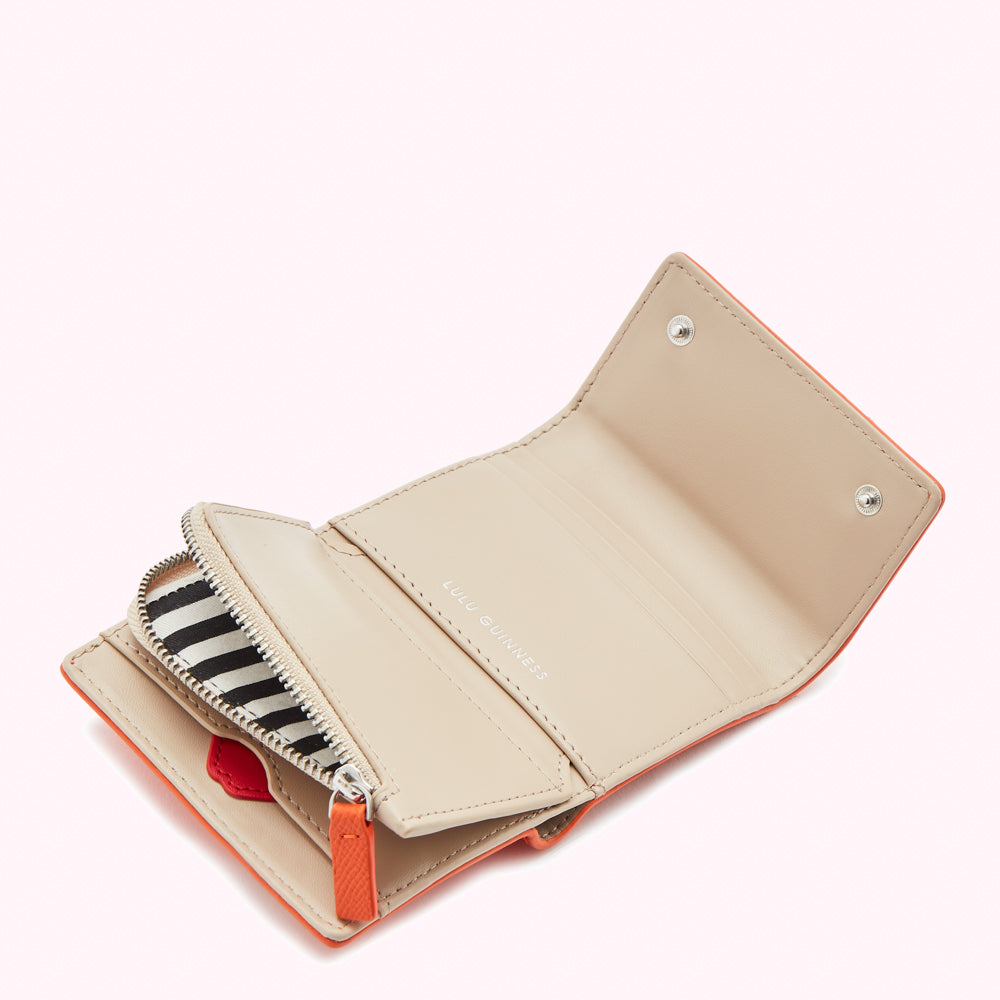Orange Lulu Guinness wallet open to reveal beige interior and black and white striped zipper.
