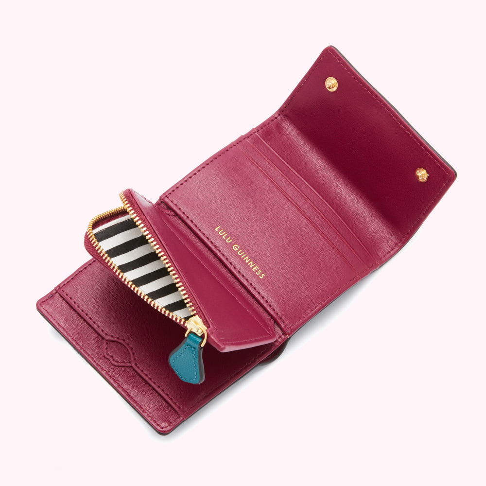 Open crimson Lulu Guinness wallet with black and white striped zipper and teal zipper pull.
