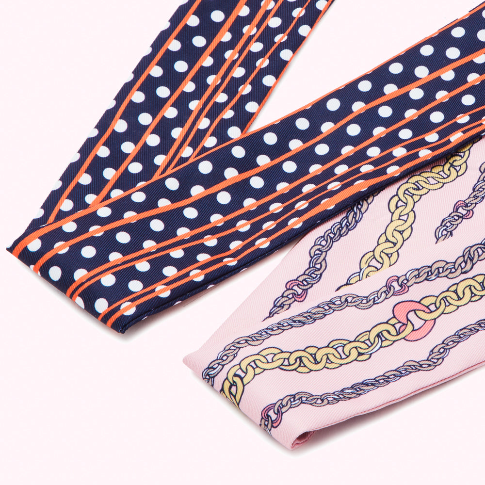 Two silk scarves, one navy blue with white polka dots and orange stripes, the other pink with a gold chain pattern.